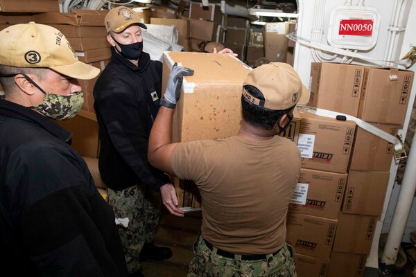 Cmdr. David Jones hands a box to Logistics Specialist 3rd Class Edgar Carreon as Senior Chief Logistics Specialist Diego Quintero verifies inventory aboard the Wasp-class amphibious assault ship USS Kearsarge (LHD 3) Dec. 10, 2020.