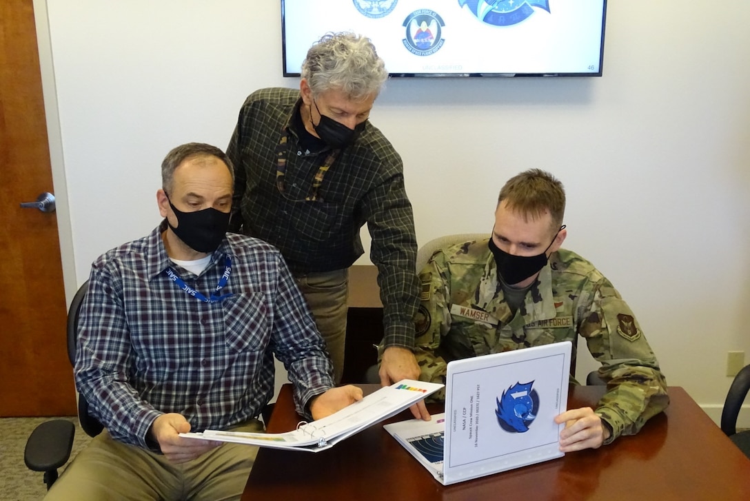 Jeff Efron (left) and Craig Diamantopoulos (middle), both space operations contractors from the Combined Force Space Component Command (CFSCC) operations directorate, look over past NASA recovery mission briefing books with Maj. Kyle Wamser, CFSCC chief of human space flight support on Dec. 7, 2020, at Vandenberg AFB, Calif. Wamser and his team most recently prepared these books for the CFSCC commander prior to the launch of the SpaceX Dragon Crew-1 ‘Resilience’ Capsule on Nov. 16, 2020, where a crew of three Americans and one Japanese astronaut launched to the International Space Station. The briefing outlines the plan for astronaut rescue operations if an emergency arises and the astronauts make an unexpected landing anywhere in the world. The CFSCC commander oversees joint and multinational military support from Vandenberg AFB and is the final authority for rescue mission execution. (U.S. Air Force photo by Lt. Col. Mae-Li Allison)