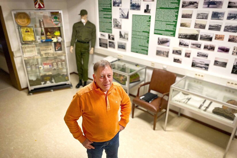 A man stands inside a room with pictures and memorabilia hanging on the walls.