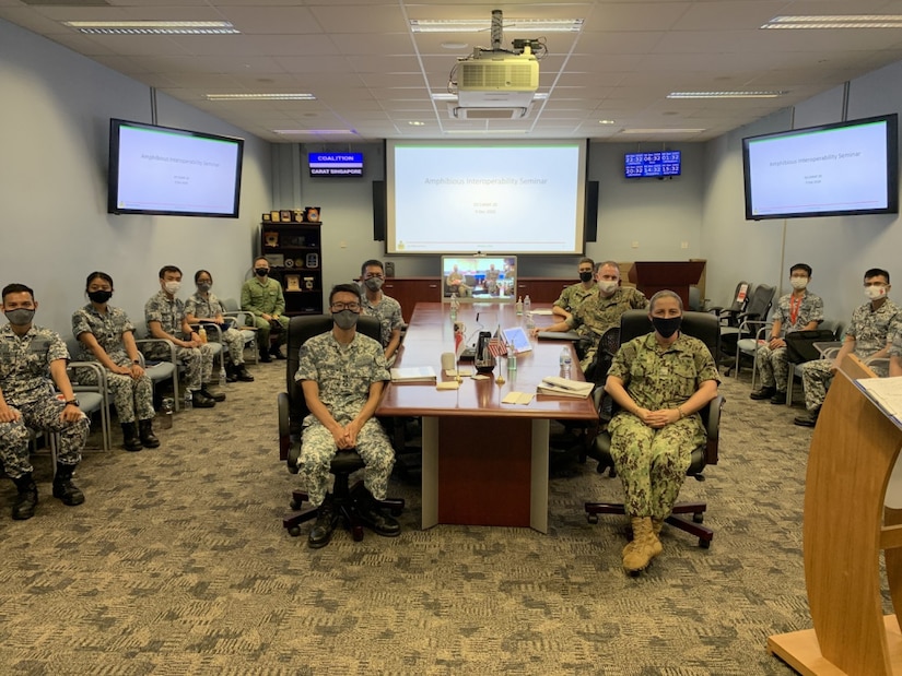 A group of service members sit around a desk and pose for a picture.