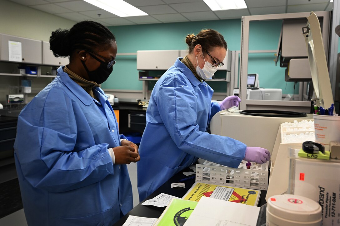 Two Air Force airmen wearing personal protective equipment record lab results.