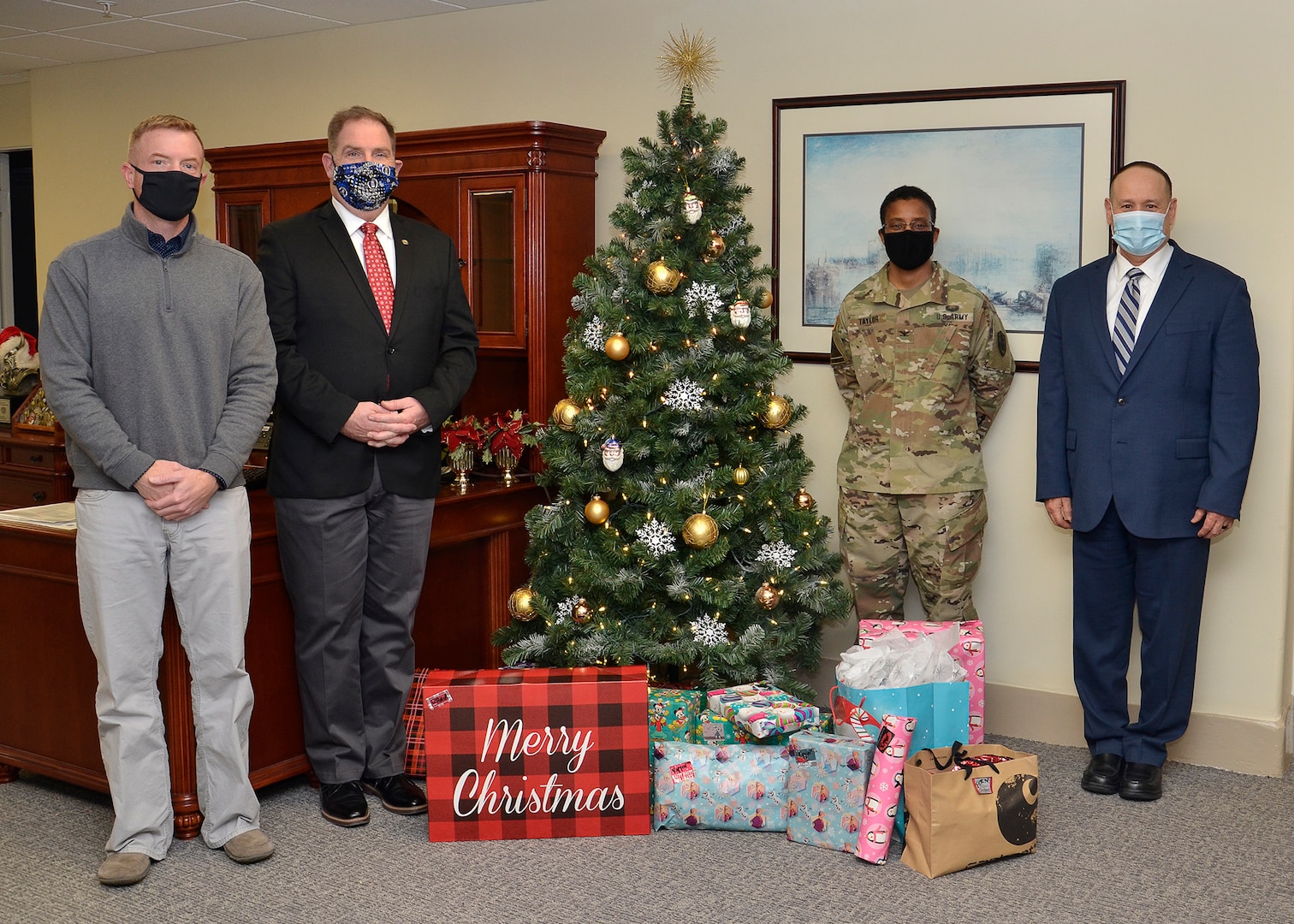 A group of four people, one of them in an Army uniform stand next to a Christmas tree in an office.
