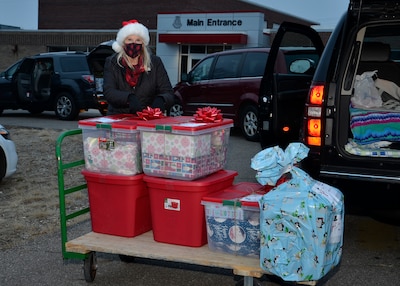 A woman stands next to a hand cart loaded with donated food and gifts for a family.