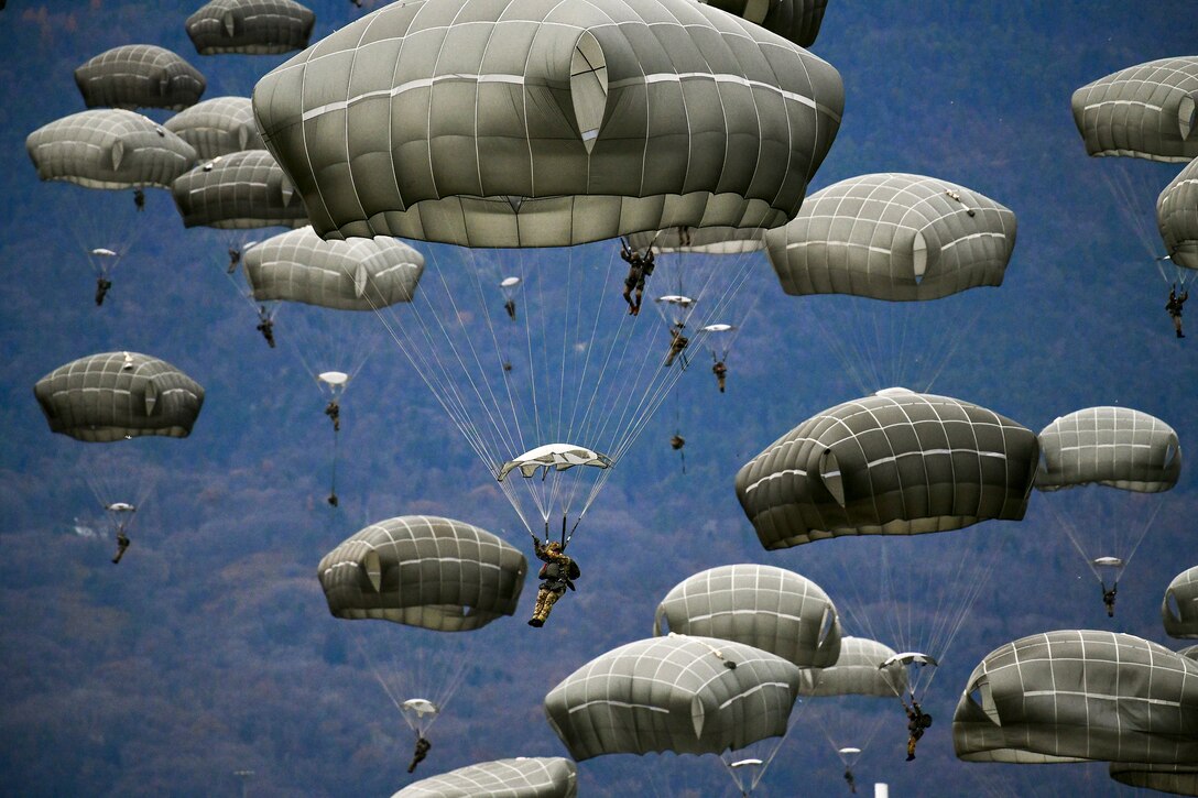 U.S. and Italian soldiers descend with deployed parachutes.
