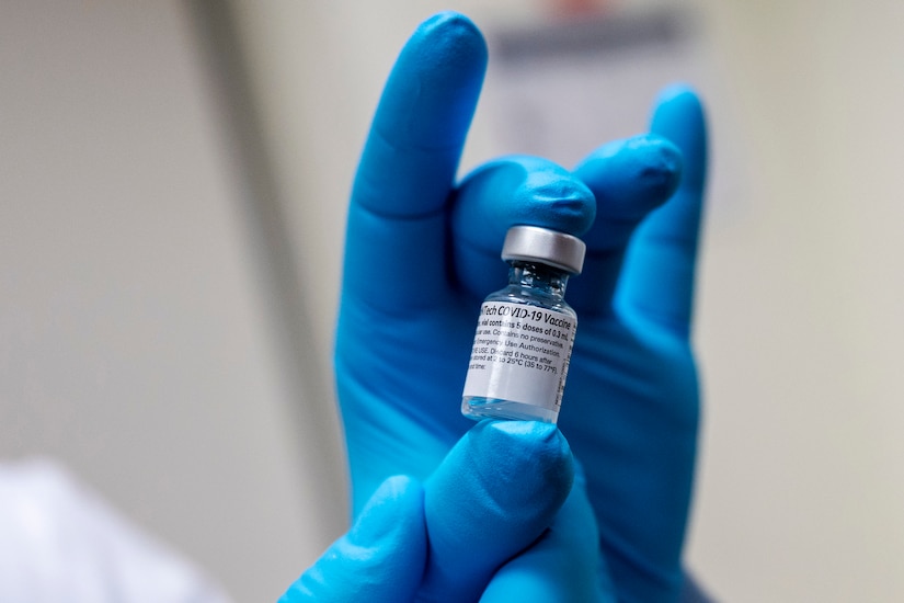 A vial of vaccine is held in gloved hands..