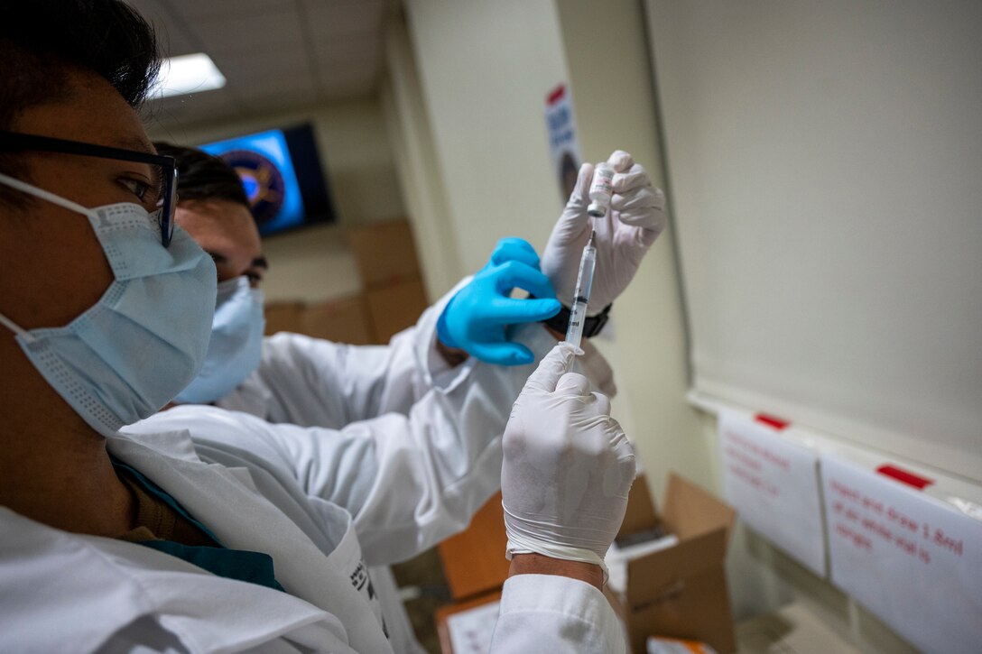 A hospital worker uses a syringe to draw fluid from a small bottle.