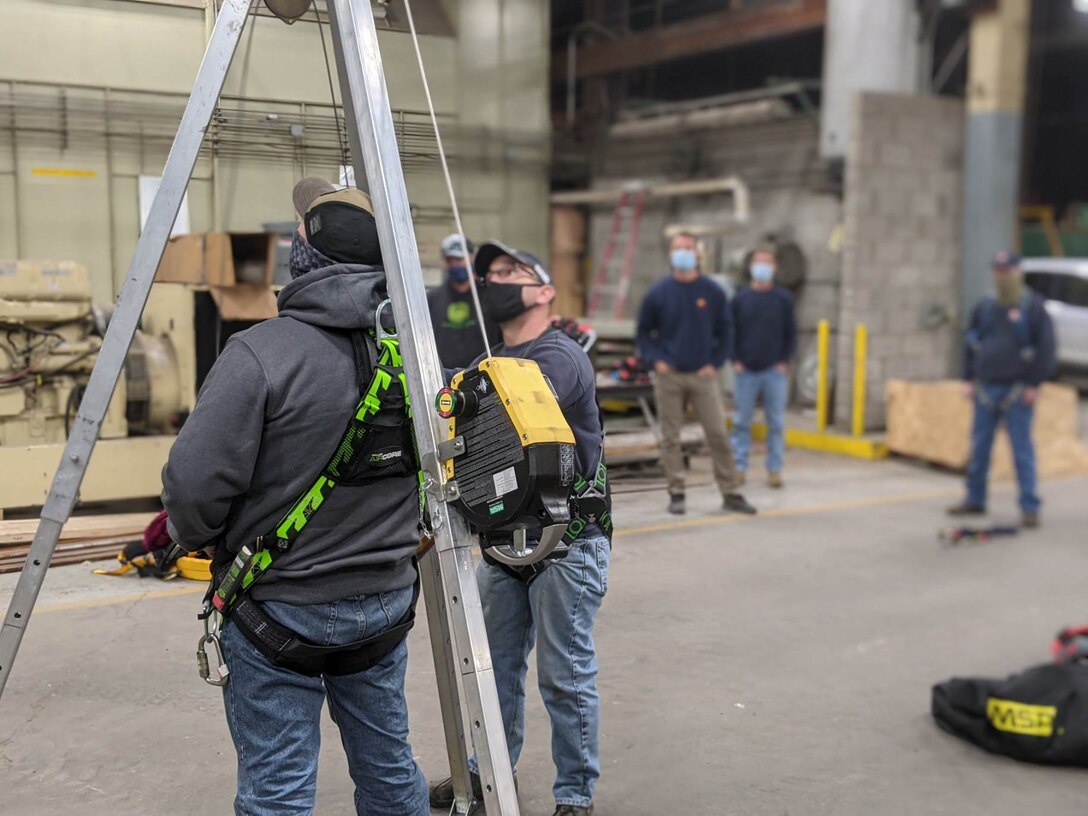 Students practice using a self-retractable lifeline and retrieval winch on a fall protection tripod.