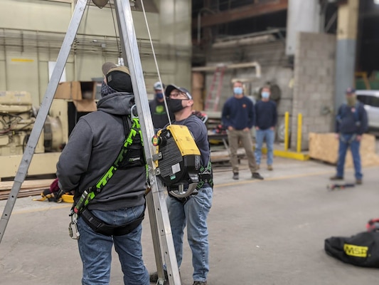 Students practice using a self-retractable lifeline and retrieval winch on a fall protection tripod.