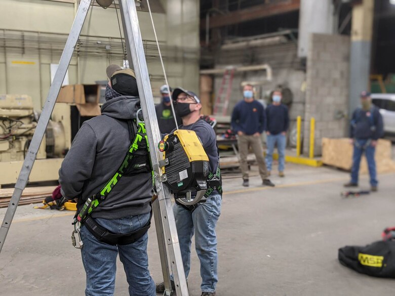 Students practice using a self-retractable lifeline and retrieval winch on a fall protection tripod.