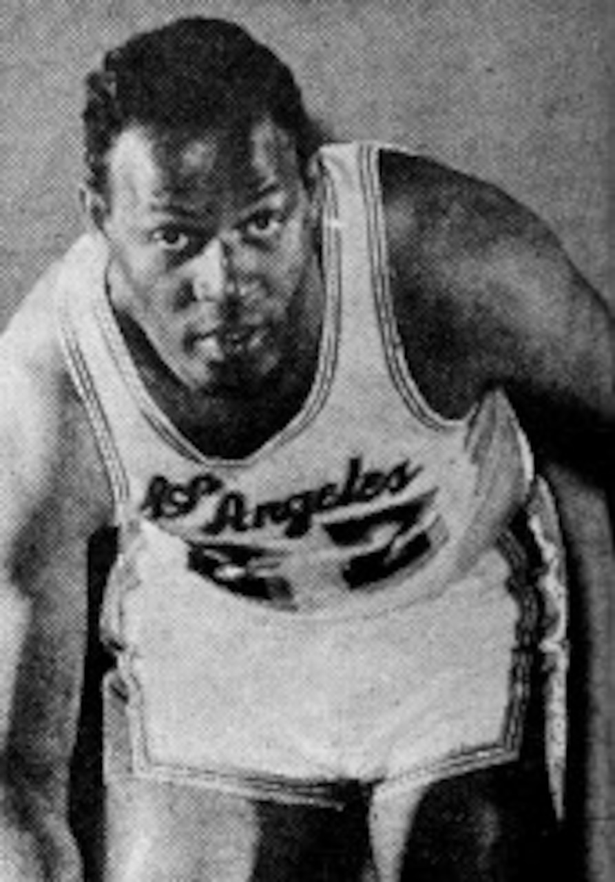 A basketball player leans forward at the waist as he dribbles the ball.