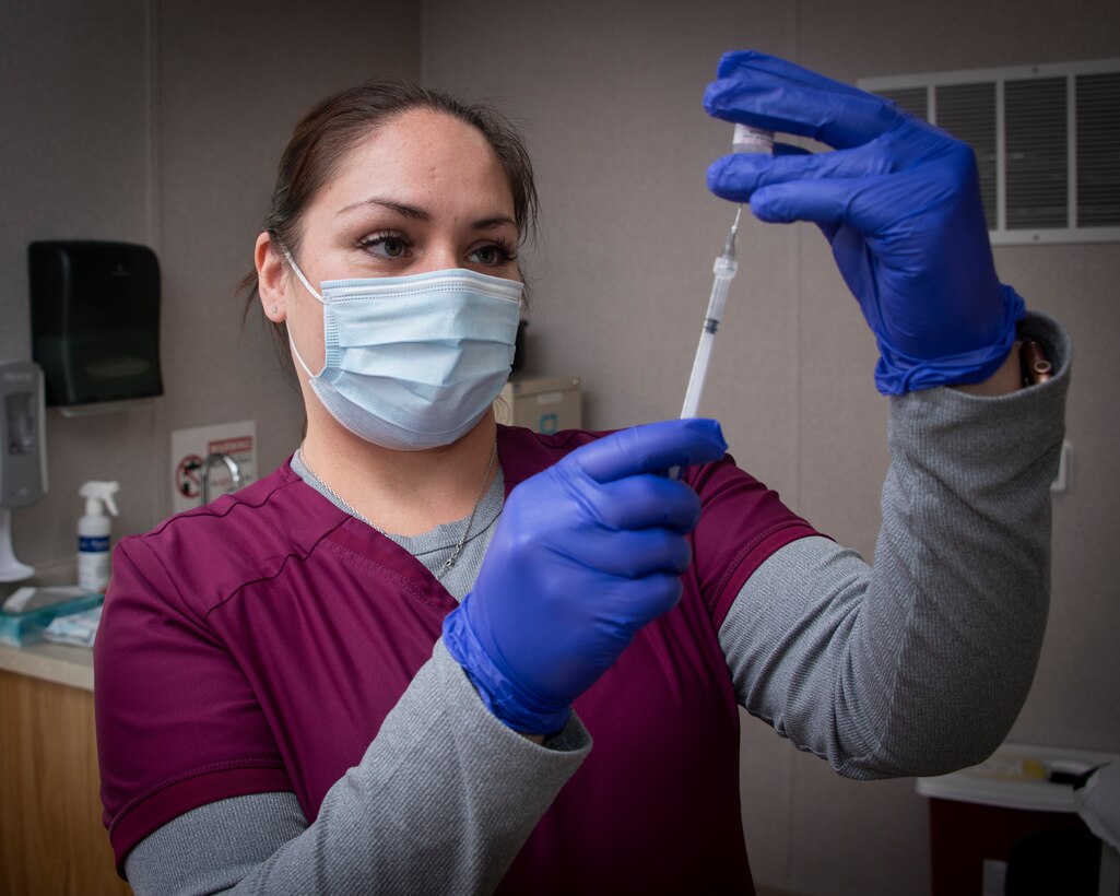 Female in nurse scrubs and a face mask and gloves prepares a needle.