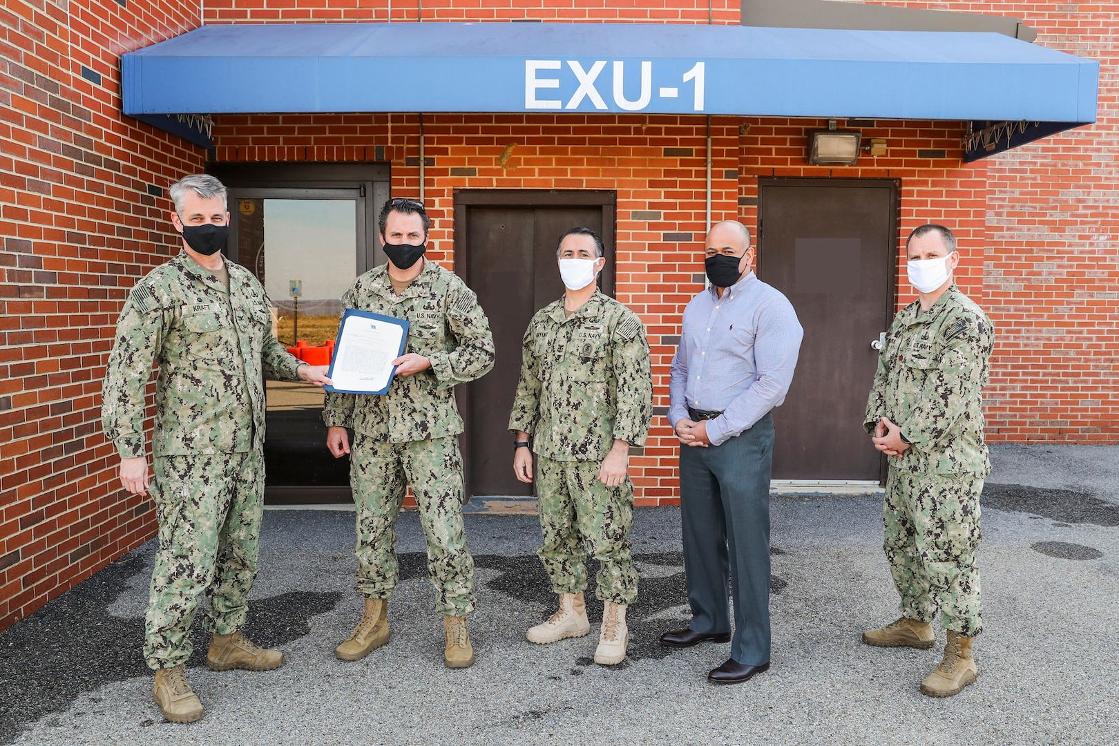 NSWC Indian Head Division Commanding Officer Capt. Scott Kraft presents EXU-1 Commanding Officer Cmdr. Edgar Britt with the Navy Unit Commendation, Dec. 15, at EXU-1’s headquarters aboard Naval Support Facility Indian Head. Also pictured are Command Master Chief Jose Bryant (center), EXU-1’s Civilian Director Alan Tompkins (center-right), and EXU-1’s Executive Officer Lt. Cmdr. Jon Maurus (right). (U.S. Navy photo by Matt Poynor)
