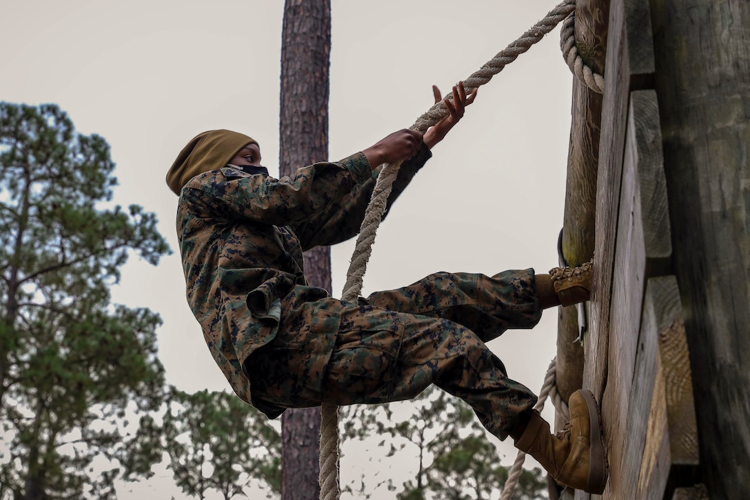 A Marine Corps recruit uses a rope to climb a wall.
