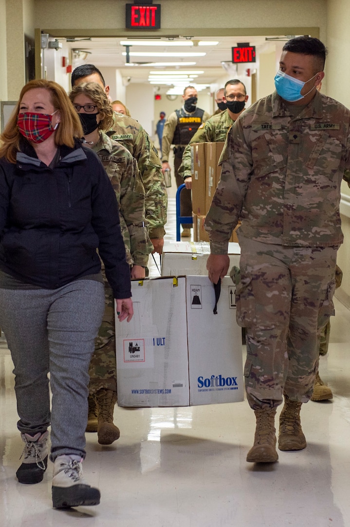 Jessica Benson, Oklahoma State Department of Health, leads Oklahoma National Guardsmen carrying boxes containing COVID-19 vaccinations to vehicles the Guard members will use to transport the vaccines to sites across the state, Dec. 15, 2020.

These are the first two boxes of vaccines to be distributed from one of five centralized hubs supporting 11 satellite locations across Oklahoma. The Guardsmen will be using Oklahoma State Department of Health vehicles to transport the vaccines to the satellite locations with an escort from the Oklahoma Highway Patrol. (Oklahoma National Guard photo by Anthony Jones)