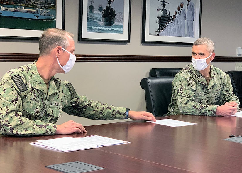 Two military leaders wearing face masks sit at a conference table.