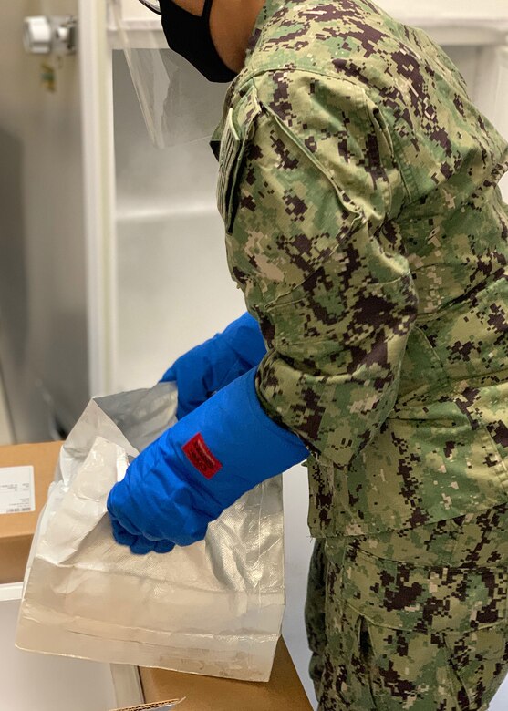 A sailor prepares to handle a box of vaccines.