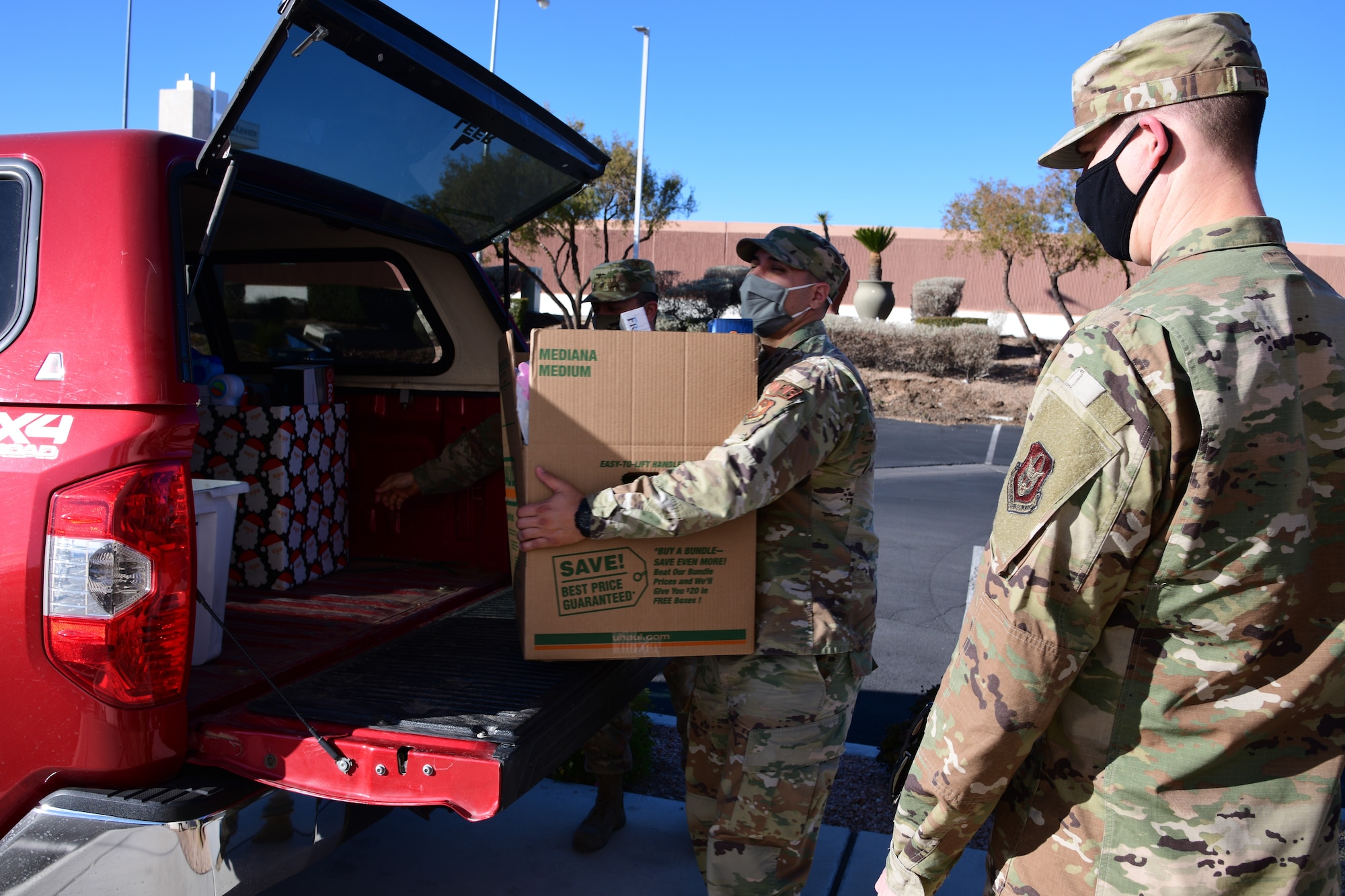 926th Wing volunteers, Master Sgt. Caleb Fishell, Tech. Sgt. Jordan Gonzales and Staff Sgt. Miguel Acosta, carry toy donations into a local nonprofit, Dec. 14, in Las Vegas, Nev. (U.S. Air Force Photo by Staff Sgt. Paige Yenke)