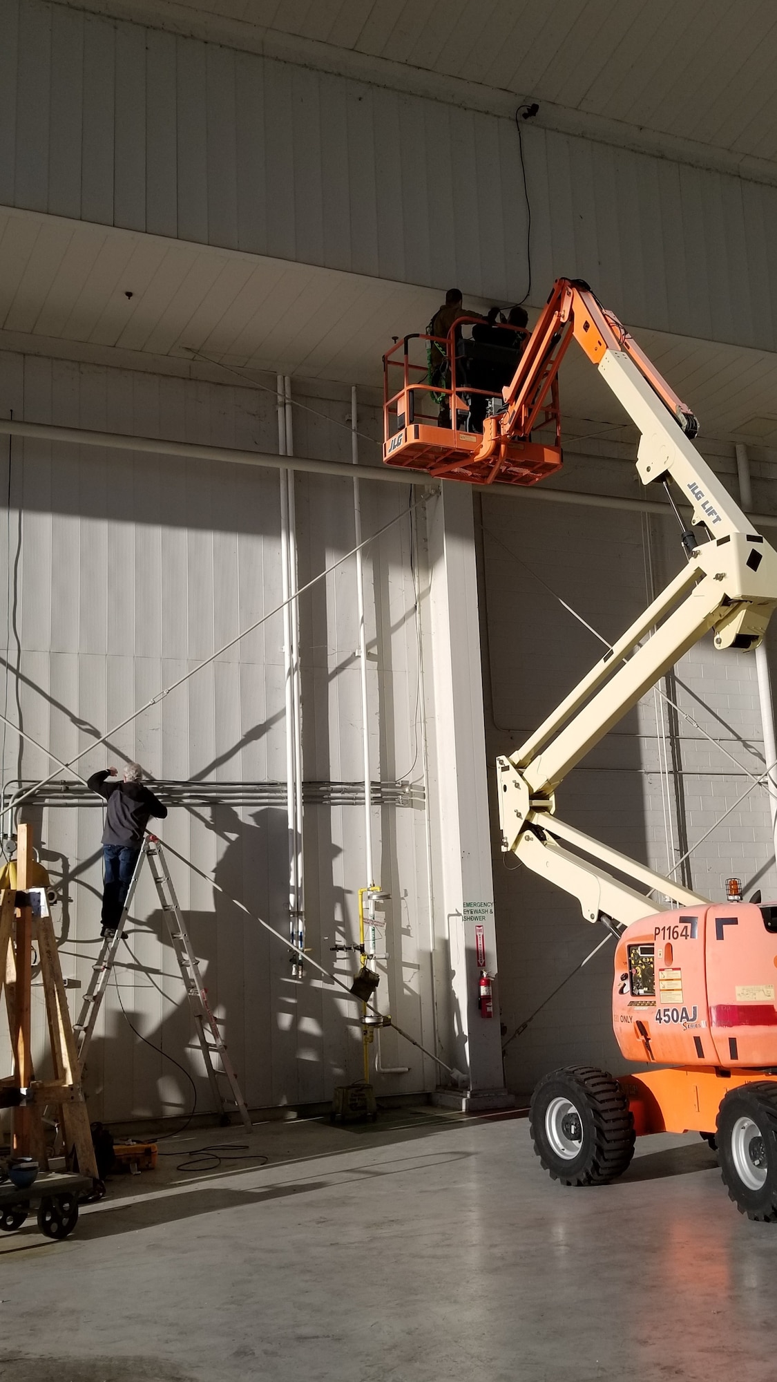 Photo shows two men in a lift drilling wires into the ceiling.