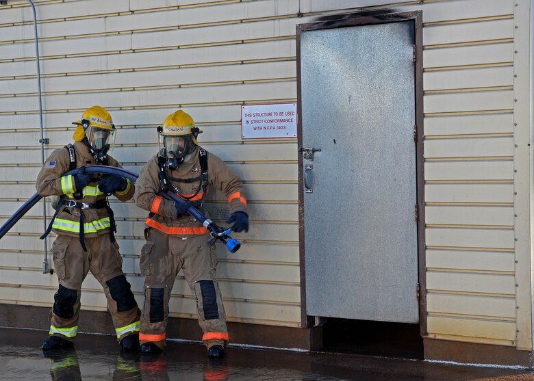 U.S. Army Pvt. Arias Caballero and Air Force Airman 1st Class Jorge Rodriquez-Aponte, 312th Training Squadron fire protection students, communicate strategy before opening the door to a burning room during their grade level interior fire training exercise at the Louis F. Garland Department of Defense Fire Academy on Goodfellow Air Force Base, Texas, Dec. 10, 2020. Students trained in the classroom how to approach a live fire and what angle to spray the water hose for different burning scenarios. (U.S. Air Force photo by Senior Airman Abbey Rieves)