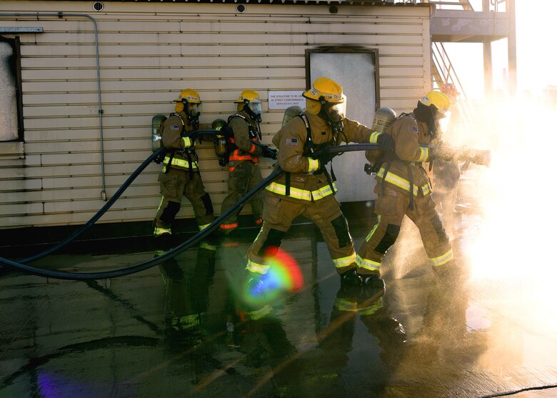 Joint service fire protection students of the 312th Training Squadron command a spraying water hose as they flex their classroom knowledge in the field during their grade level interior fire training exercise at the Louis F. Garland Department of Defense Fire Academy on Goodfellow Air Force Base, Texas, Dec. 10, 2020. The 312th TRS students participated in hands-on training and used the “buddy system,” to control unpredictable visibility challenges presented in their educational environment. (U.S. Air Force photo by Senior Airman Abbey Rieves)