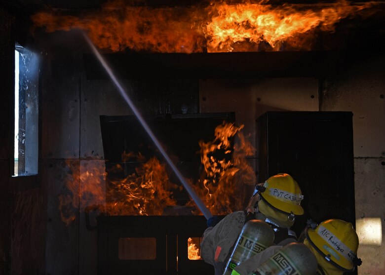 U.S. Army Pvt. Arias Caballero and Air Force Airman 1st Class Jorge Rodriquez-Aponte, 312th Training Squadron fire protection students, extinguish the burning room together during their grade level interior fire training exercise at the Louis F. Garland Department of Defense Fire Academy on Goodfellow Air Force Base, Texas, Dec. 10, 2020.  The students were assigned to three units which all had different roles to play during a structure fire. (U.S. Air Force Senior Airman Abbey Rieves)