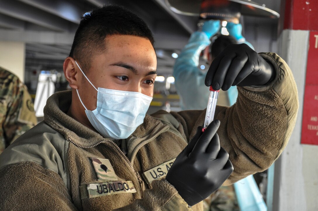 A soldier wearing a face mask inspects a sample tube.