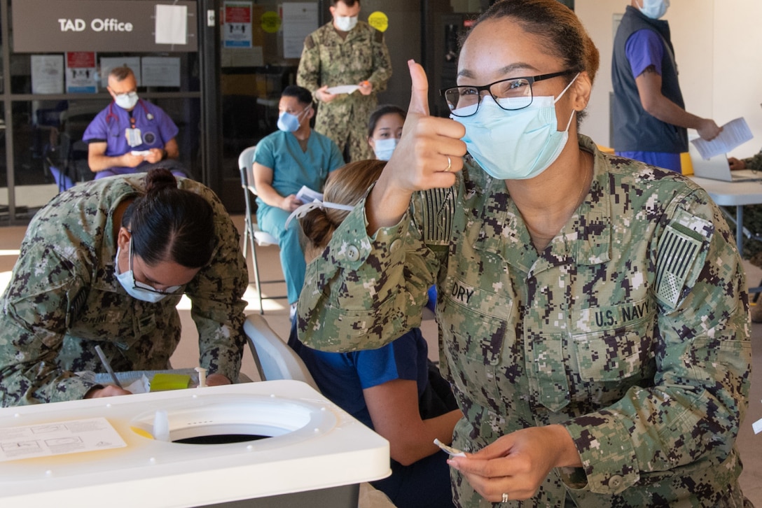 A Navy seaman wearing a face mask gives a thumbs up after she finishes completing paperwork for a COVID-19 vaccine.
