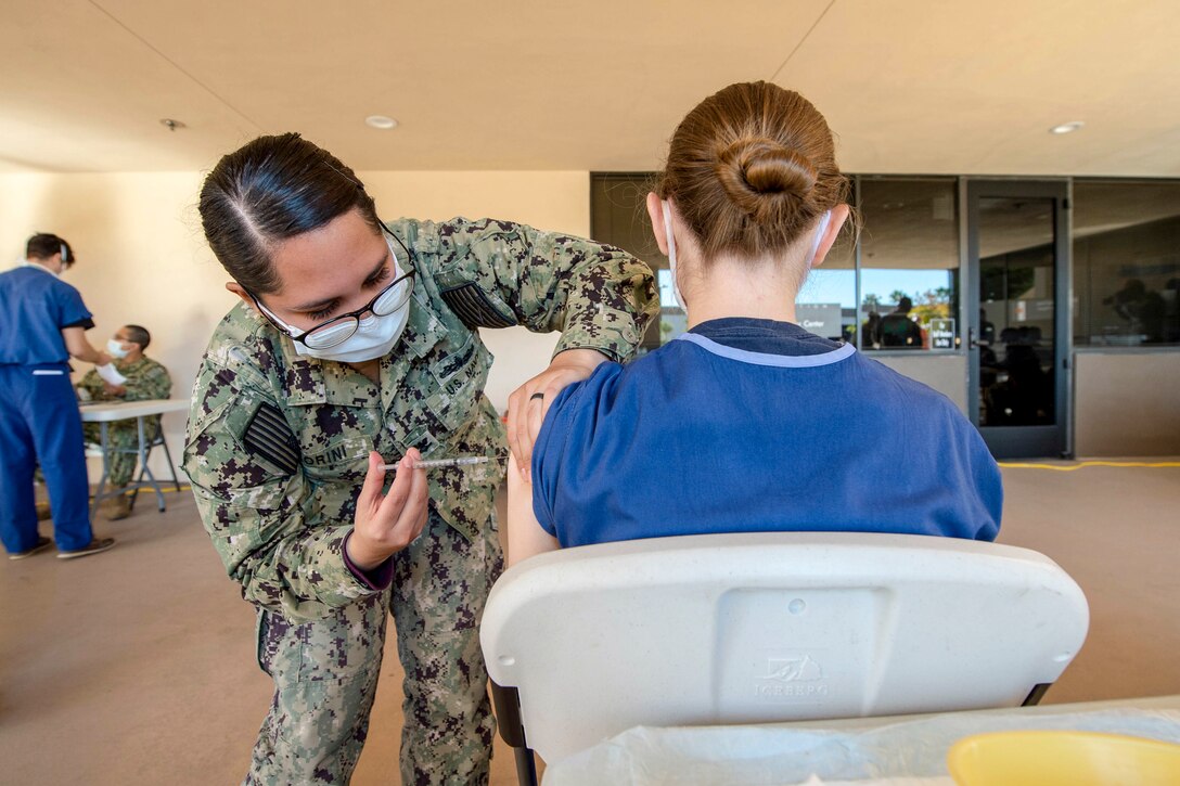 A Navy seaman wearing a face mask vaccinates a volunteer with a COVID-19 vaccine.