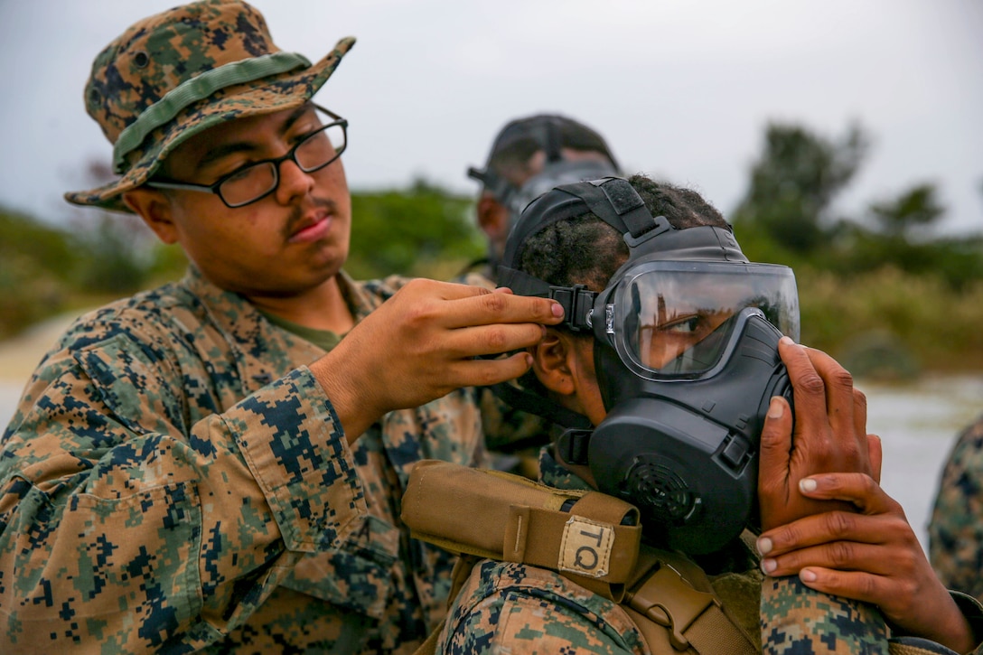 One Marine helps another adjust her gas mask.