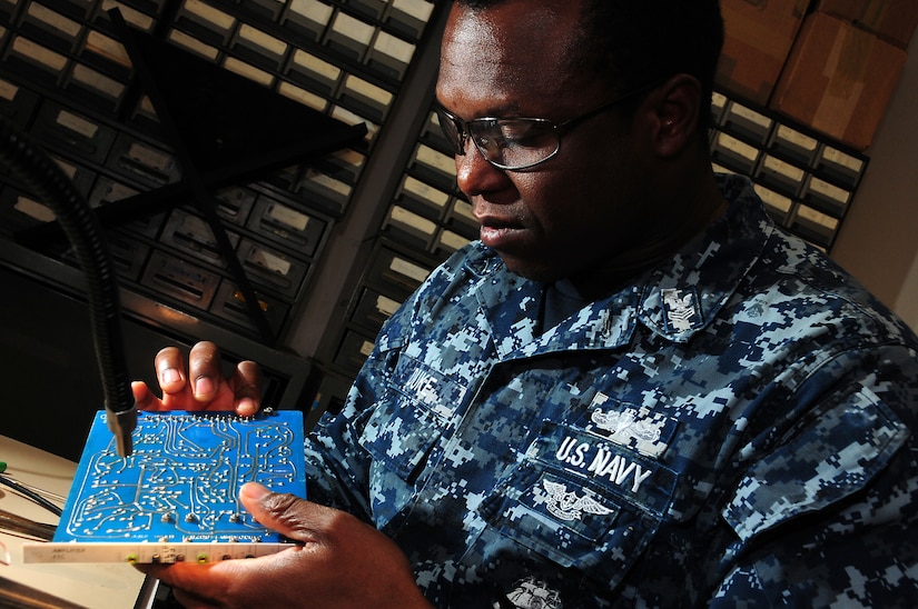 A man in a uniform inspects a circuit board.