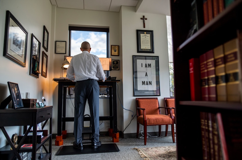 A man works at a standing desk by a window in an office.