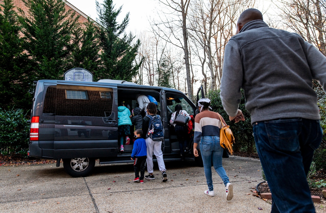 A man walks toward a van as kids climb into it.