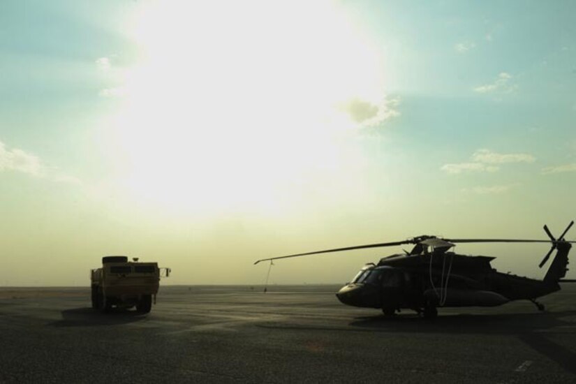 A helicopter and a vehicle sit on the desert floor.