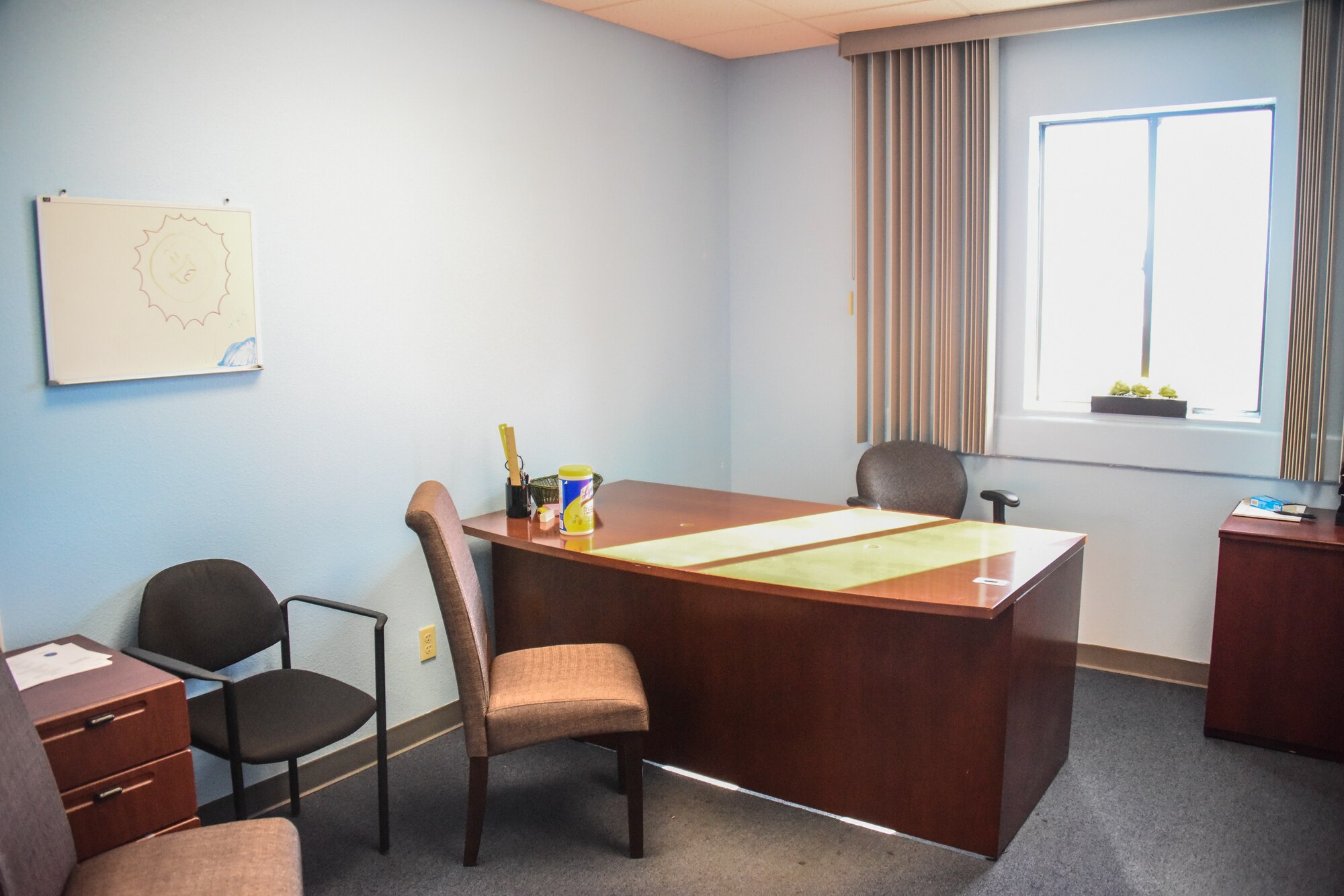 A picture of a blue room with worn furniture, and a desk in the middle.