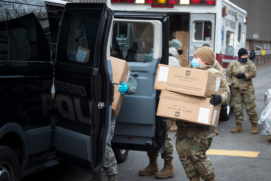Soldiers wearing face masks and gloves load boxes of personal protective equipment into vehicles.
