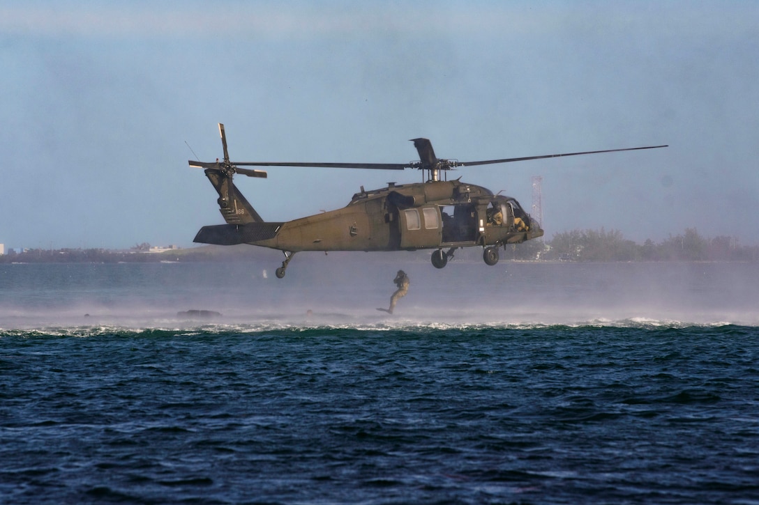 A soldier jumps from a helicopter into a body of water.