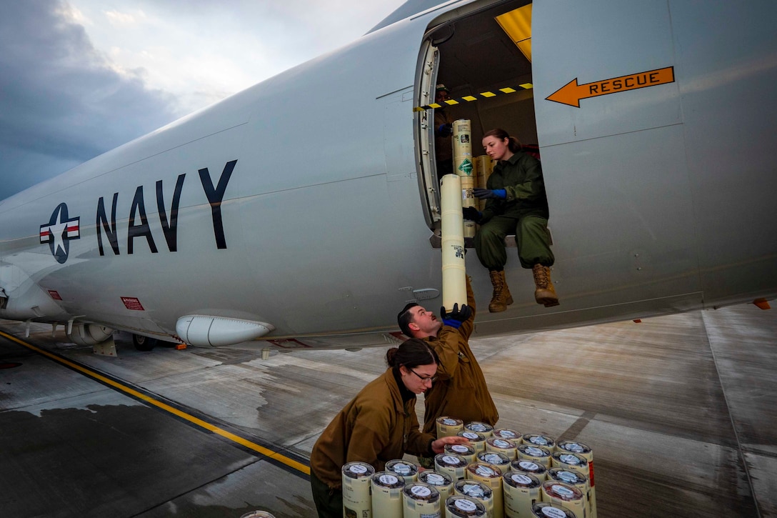A sailor sits inside an aircraft as two others hand her sonobuoys to load into the aircraft.