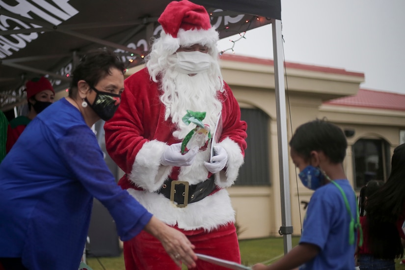A woman helps Santa give gifts.