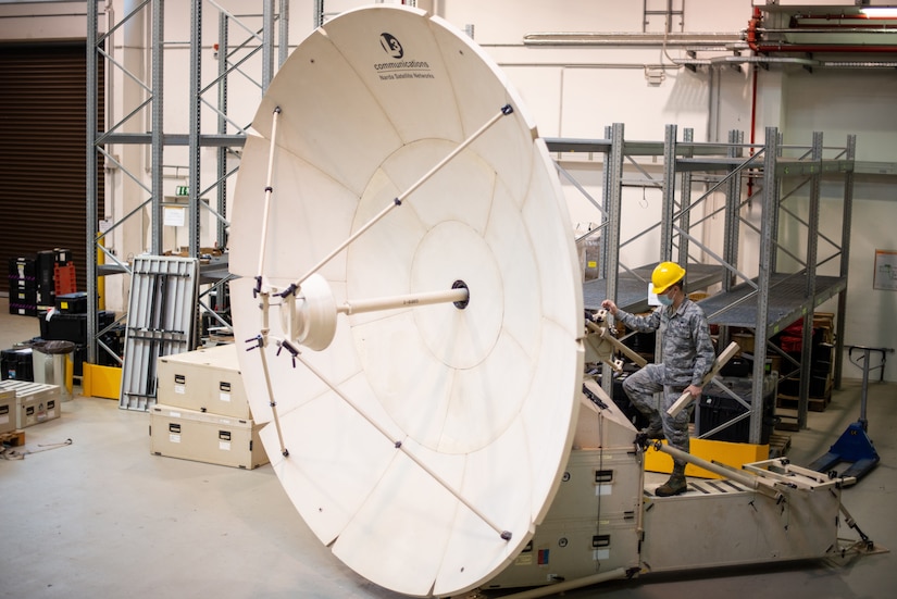 A man works on a large satellite inside a warehouse.