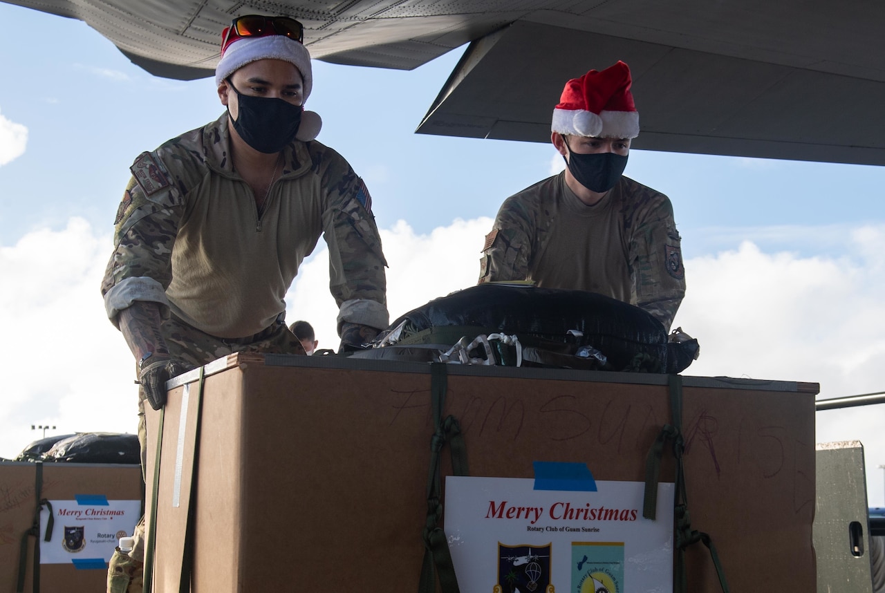 Two service members wearing Santa hats load a large box into a plane.