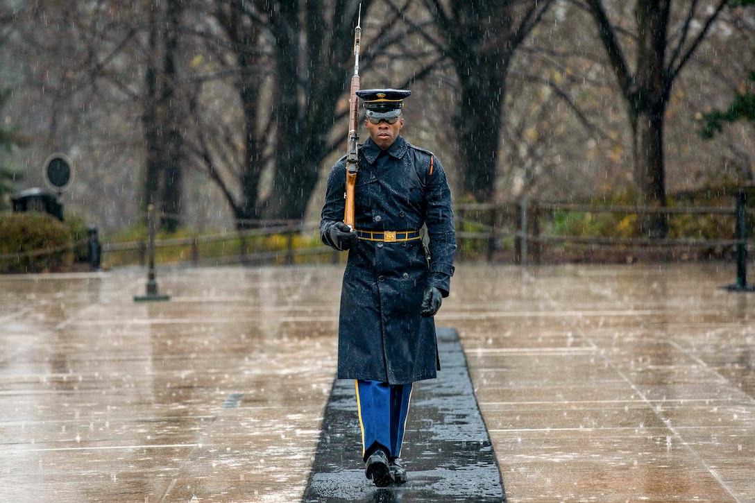 A soldier walks on a mat outside in pouring rain.