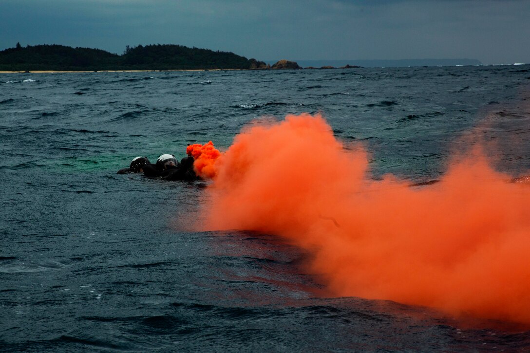 A Marine swims in a body of water near a cloud of orange smoke.