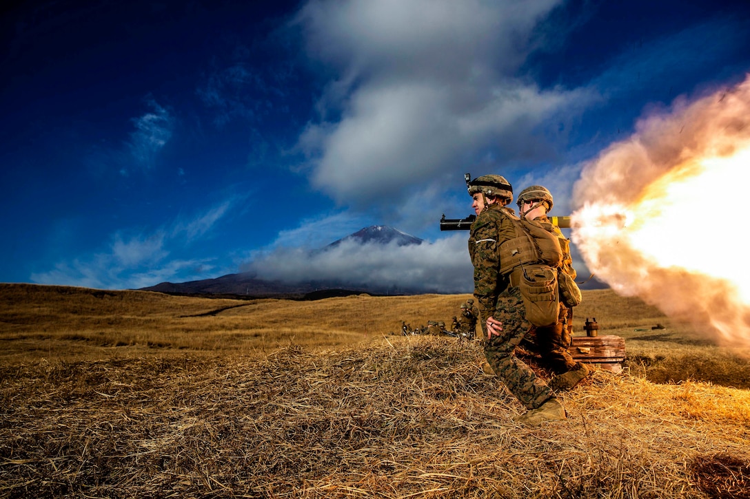 Marines fire a weapon near mountains.