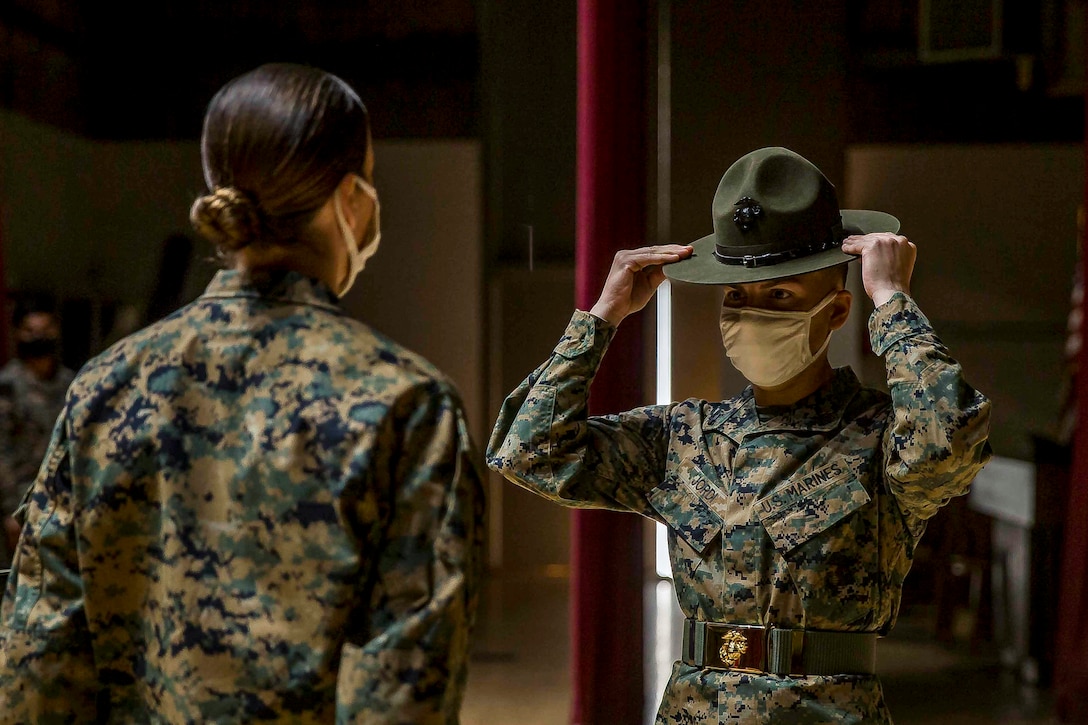 A Marine adjusts his drill instructor hat while another stands facing him.
