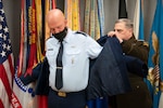 A man in a military uniform helps another man put on a jacket.