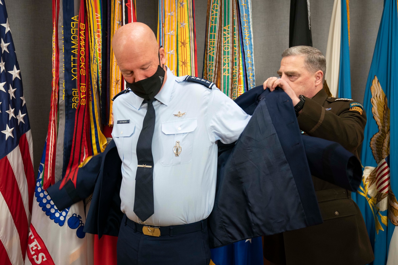 A man in a military uniform helps another man put on a jacket.