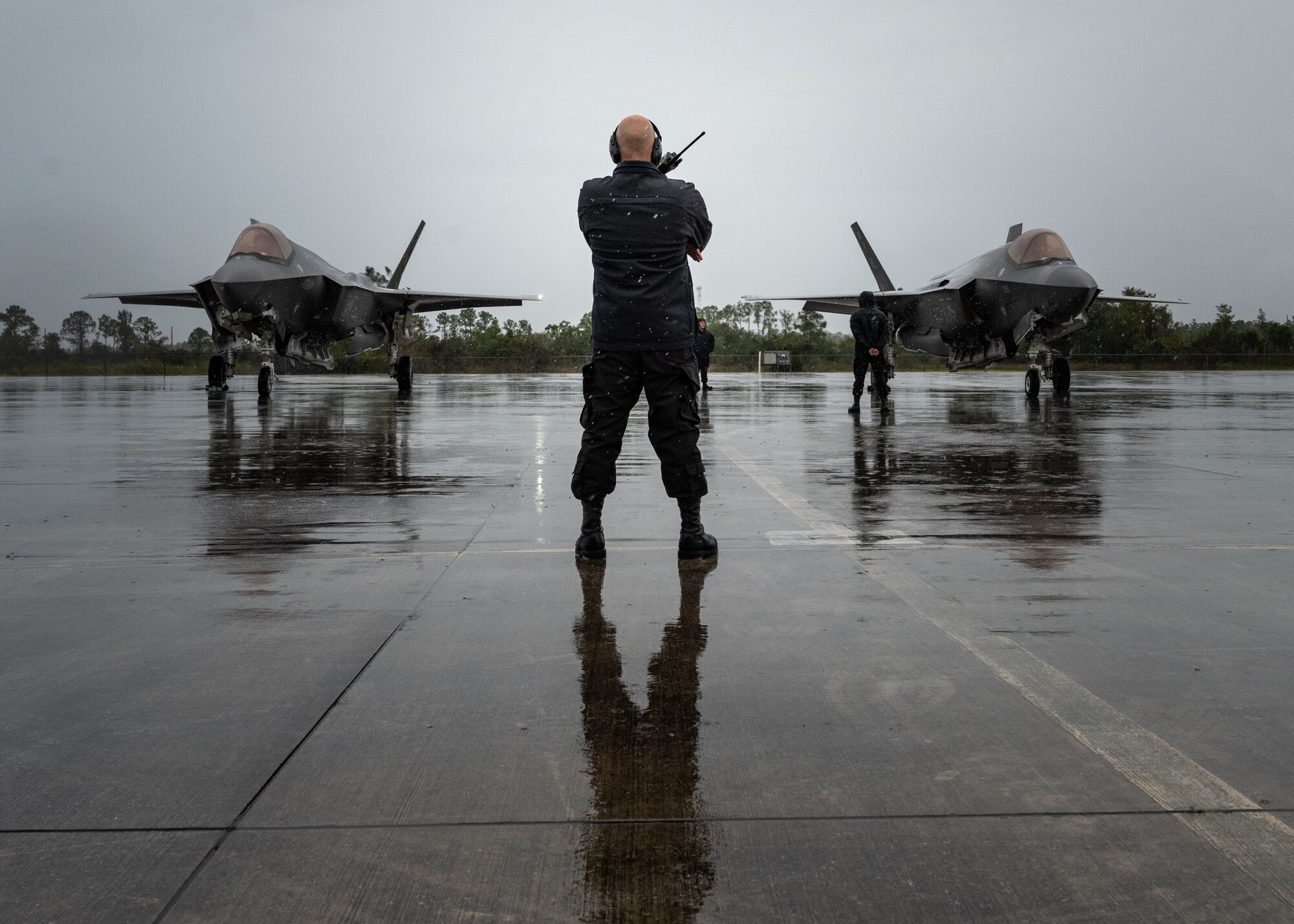 An F-35A Demonstration Team Maintainer stands before two F-35A Lightning IIs prior to take-off.