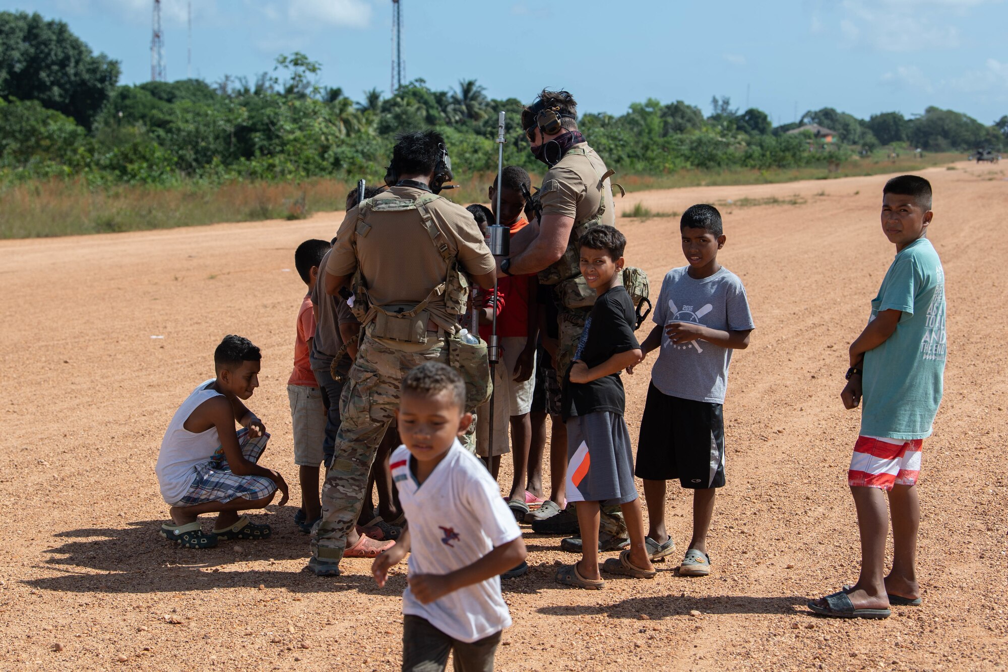 A group of Honduran children have gathered around a pair of Special Tactics operators driving a pole into the ground to measure its hardness.