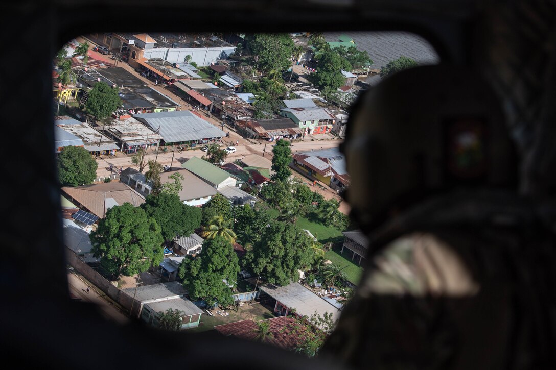 We look out a window over the shoulder of a Special Tactics operator at the city going by far below.