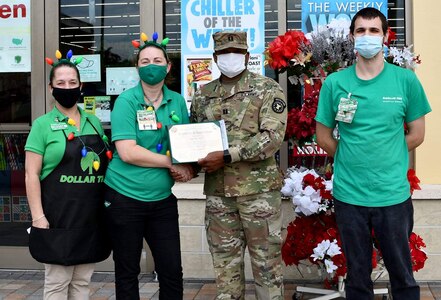 A man in military uniform presents a certificate to three store employees